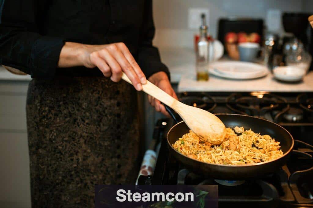A woman stirs a delicious rice dish in a frying pan on a gas stove with a wooden spoon.